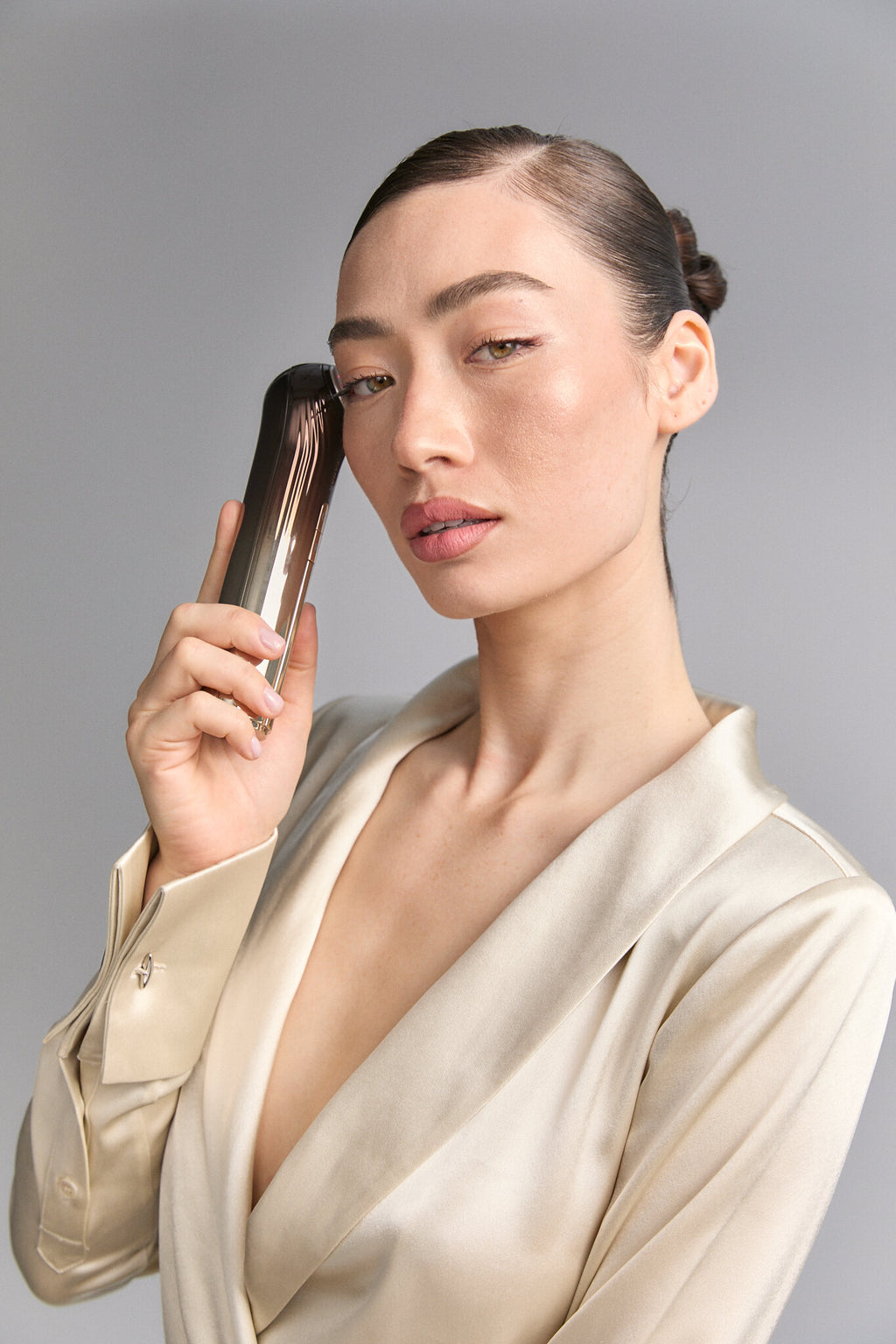 Model holding Bloom 6 to her temple, cream satin blouse