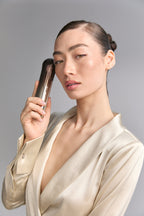 Model holding Bloom 6 to her temple, cream satin blouse