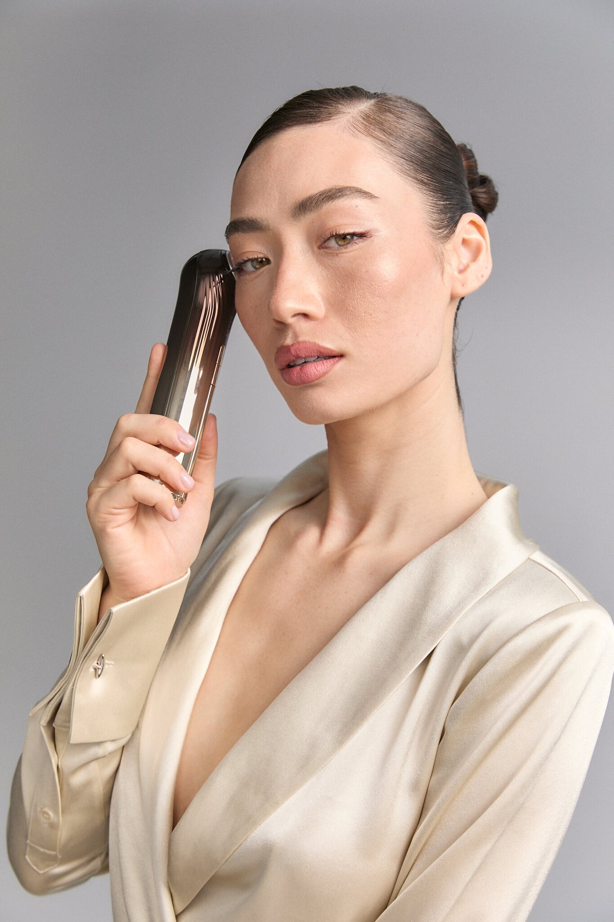 Model holding Bloom 6 to her temple, cream satin blouse