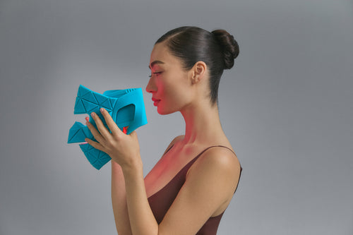 Model in profile holding the Blue Green Mask Lift in teal, red light on